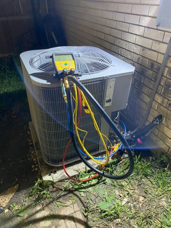 Air conditioner condenser being diagnosed with digital manifold gauges at night