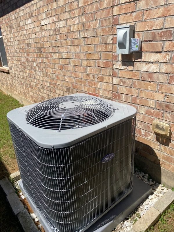 Clean Carrier air conditioning condenser installed on a pad beside a brick home