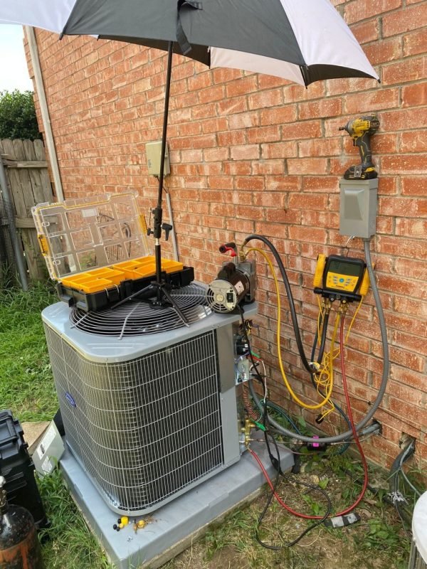 HVAC technician tools, vacuum pump and gauges set up on a condenser during a tune-up